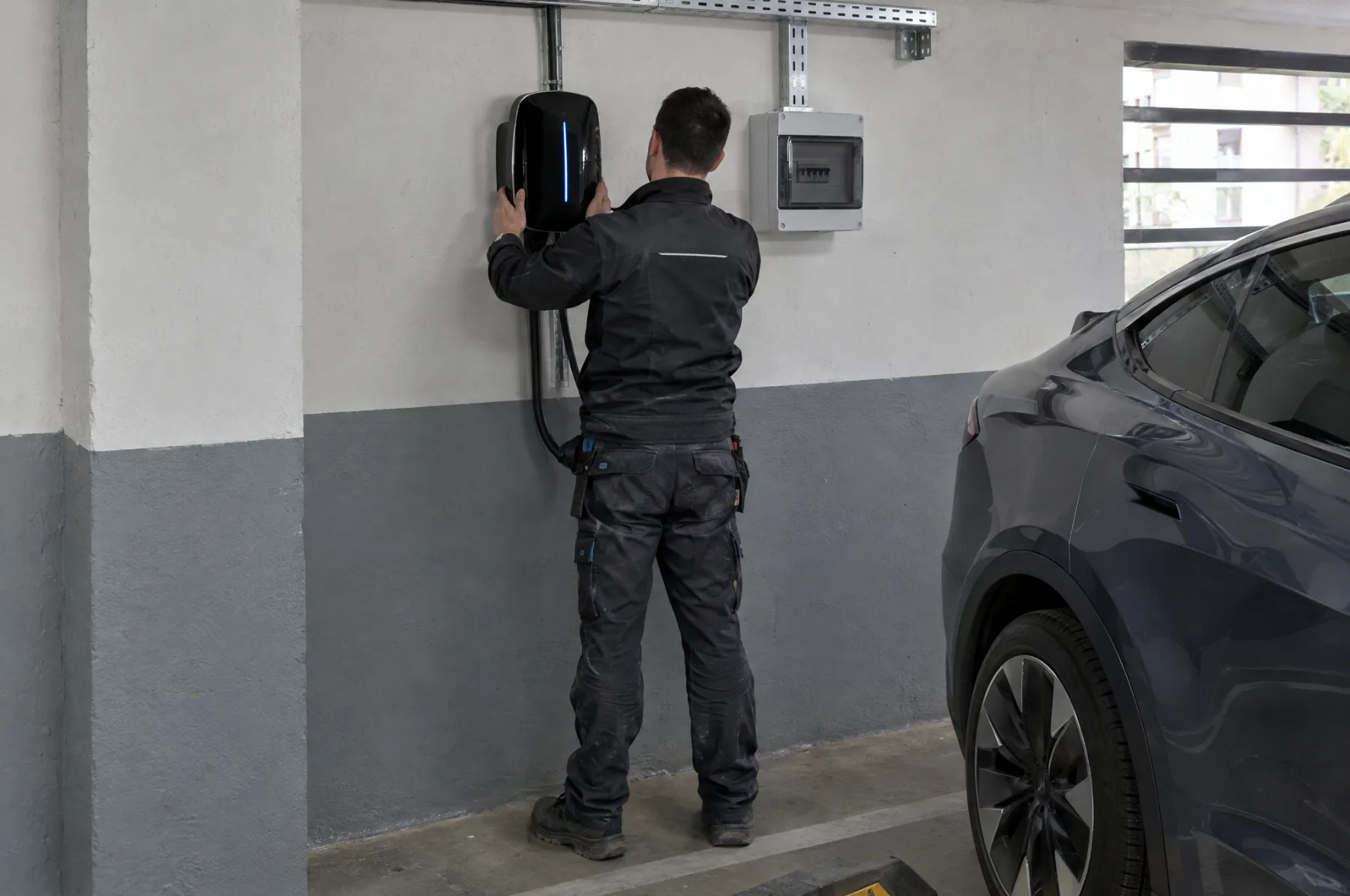 An electrician installing a wall charger in an apartment building garage
